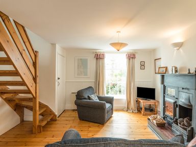 A living room with wooden staircase grey armchairs a television and a fireplace at 3B Coastguard Cottages in Low Newton-By-The-Sea