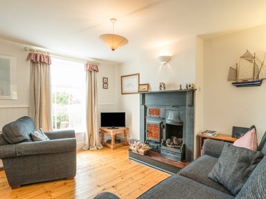 A living room with two sofas a fireplace a small TV and curtains at 3B Coastguard Cottages Low Newton-By-The-Sea