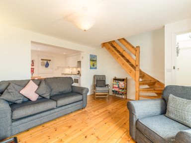 A sitting area with two sofas a chair wooden stairs and a book rack at 3B Coastguard Cottages in Low Newton-By-The-Sea