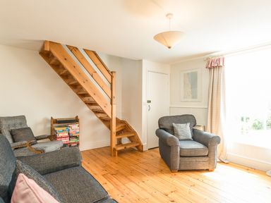 A living room with wooden stairs a gray armchair and a gray sofa at 3B Coastguard Cottages in Low Newton-By-The-Sea
