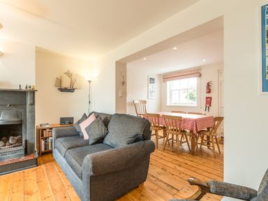 A living room with a sofa, a fireplace, a floor lamp, and a dining area with a table covered with a checkered tablecloth at 3B Coastguard Cottages in Low Newton-By-The-Sea
