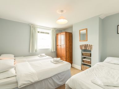 A bedroom with three single beds a wooden wardrobe and shelves with baskets at 3B Coastguard Cottages in Low Newton-By-The-Sea
