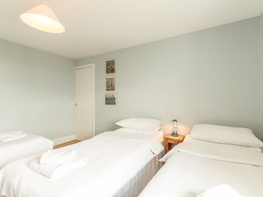 A bedroom with two single beds white bedding a wooden nightstand with a lamp and three framed pictures on the wall at 3B Coastguard Cottages in Low Newton-By-The-Sea