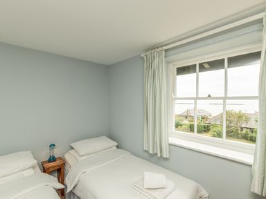 A bedroom with two single beds a small wooden side table with a blue lamp and a window with striped curtains at 3B Coastguard Cottages in Low Newton-By-The-Sea