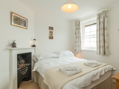A bedroom with a double bed towels on it a window with curtains and a fireplace at 3B Coastguard Cottages in Low Newton-By-The-Sea