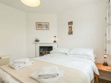 A bedroom with a double bed bedside tables towels and framed pictures on the walls at 3B Coastguard Cottages in Low Newton-By-The-Sea