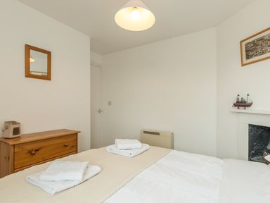 A bedroom with a bed with folded towels a wooden dresser a wall mirror and a model boat on a shelf at 3B Coastguard Cottages in Low Newton-By-The-Sea
