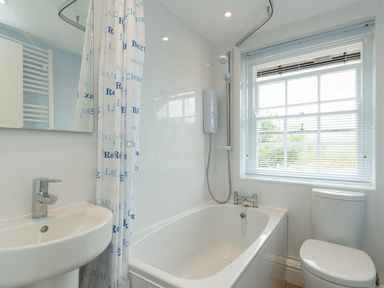 A bathroom with a bathtub shower combination sink and toilet next to a window with blinds at 3B Coastguard Cottages in Low Newton-By-The-Sea