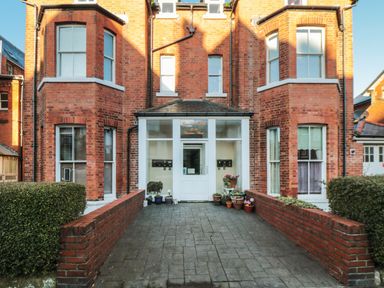 Entrance to a red brick building with potted plants on either side of a paved walkway at Carisbrooke House Apartment 6 in Scarborough