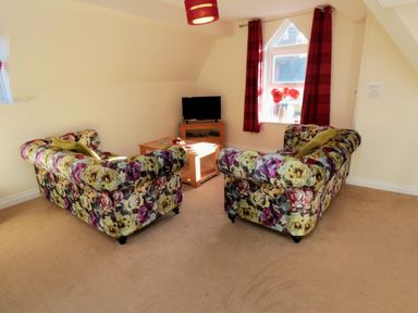 A sitting area with floral patterned sofas, a wooden coffee table, a small TV on a stand, and a window with red curtains at Carisbrooke House, Apartment 6 in Scarborough