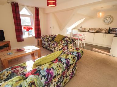 A living room with floral sofas a wooden coffee table and a kitchen area at Carisbrooke House Apartment 6 in Scarborough