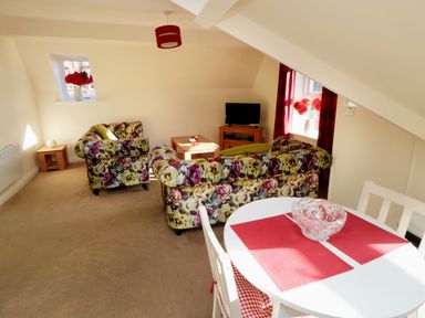 A living room with floral sofas a small tv on a wooden stand a coffee table and a dining table with red placemats at Carisbrooke House Apartment 6 in Scarborough