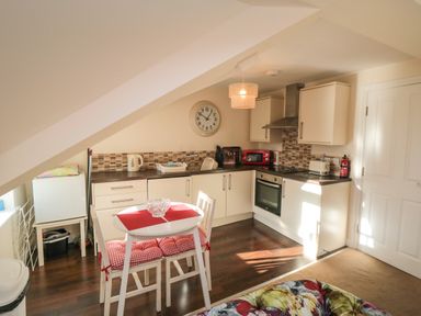 A kitchen with white cabinets a dining table with two chairs and red cushions and a clock on the wall at Carisbrooke House Apartment 6 in Scarborough