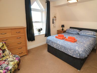 A bedroom with a double bed a wooden chest of drawers a floral armchair and a window with curtains at Carisbrooke House Apartment 6 in Scarborough