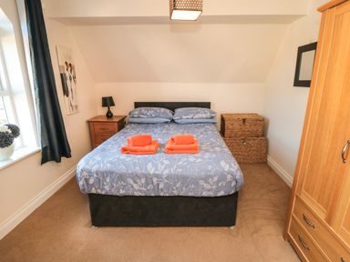 A bedroom with a double bed with blue bedding and orange towels two wicker storage baskets wooden wardrobe and nightstand with lamp at Carisbrooke House Apartment 6 in Scarborough