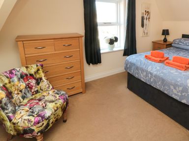 A bedroom with a bed with orange towels on it a wooden chest of drawers a floral chair and a window with curtains at Carisbrooke House Apartment 6 Scarborough
