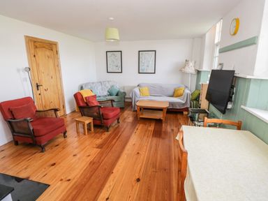 A living room with two red armchairs green and gray sofas wooden coffee table TV on wall and dining table at The Old School House in Gortermone near Carrigallen County Leitrim