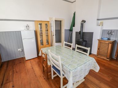 A dining room with a wooden table covered by a patterned tablecloth surrounded by chairs a refrigerator a glass cabinet and a wood stove at The Old School House in Gortermone near Carrigallen County Leitrim