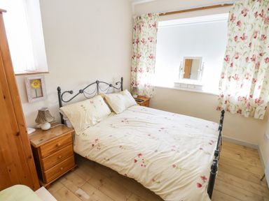 A bedroom with a bed with floral bedding, wooden nightstands with lamps, floral curtains, and a vanity mirror on the windowsill at The Old School House in Gortermone near Carrigallen County Leitrim