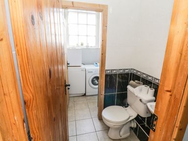 A small bathroom with a toilet and washing machine next to a window at The Old School House Gortermone near Carrigallen County Leitrim
