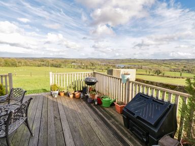 A wooden deck with potted plants a barbecue grill and outdoor chairs overlooking a rural landscape at The Old School House in Gortermone near Carrigallen County Leitrim