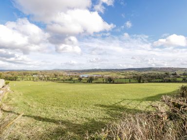 A grassy field with sheep and distant trees under a partly cloudy sky at The Old School House in Gortermone near Carrigallen County Leitrim