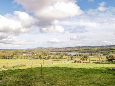A rural landscape with green fields and scattered trees under a partly cloudy sky at The Old School House in Gortermone near Carrigallen County Leitrim