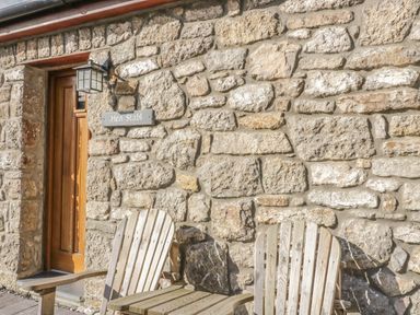 A stone wall with a wooden door and two wooden chairs outside at Hen Stabl Llangoed near Beaumaris