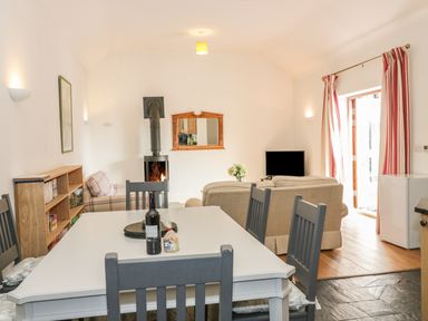 A dining area with a table and chairs next to a living room with sofas a fireplace and a television at Hen Stabl in Llangoed near Beaumaris
