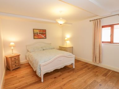 A bedroom with a double bed two bedside tables with lamps a window with curtains and a painting on the wall at Hen Stabl in Llangoed near Beaumaris