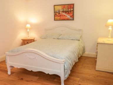 A bedroom with a wooden double bed with floral bedding two bedside tables with lamps and a painting above the bed at Hen Stabl in Llangoed near Beaumaris