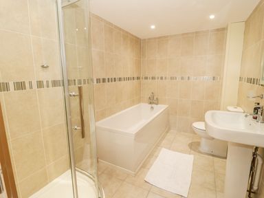 A bathroom with a bathtub shower toilet sink and a white mat on the floor at Hen Stabl in Llangoed near Beaumaris