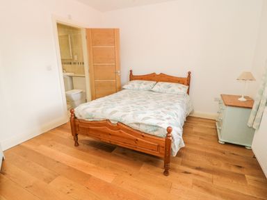 A bedroom with a wooden double bed a bedside table with a lamp and an en suite bathroom at Hen Stabl in Llangoed near Beaumaris