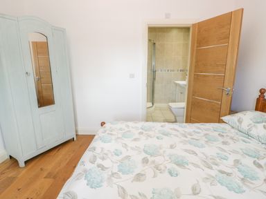 A bedroom with a bed with floral bedding a light blue wardrobe and an open door leading to a bathroom at Hen Stabl in Llangoed near Beaumaris