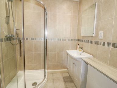A bathroom with a corner shower enclosure a sink with a cabinet a mirror and tiled walls at Hen Stabl in Llangoed near Beaumaris