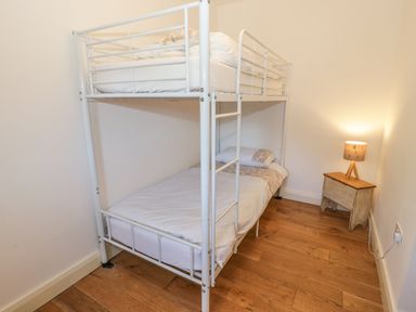 A bedroom with a white metal bunk bed a wooden floor and a small wooden side table with a lamp at Hen Stabl in Llangoed near Beaumaris