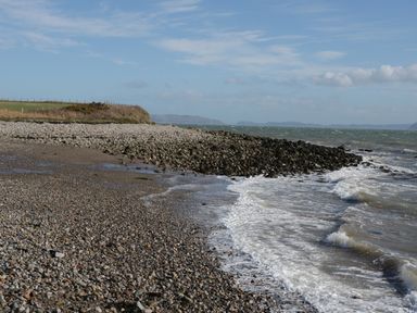 A rocky beach with waves hitting the shore and grassy land with a fence in the background at Hen Stabl Llangoed near Beaumaris