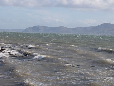 A view of choppy sea water with hills in the background at Hen Stabl in Llangoed near Beaumaris