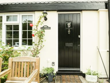 The entrance of a house with a black door and window beside wooden chair and plants at Wye Valley Cottage in Symonds Yat