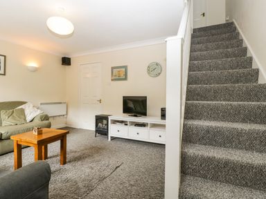 A living room with sofas a wooden coffee table a television on a white stand and carpeted stairs at Wye Valley Cottage in Symonds Yat