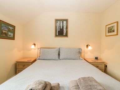A bedroom with a bed two bedside tables lamps and framed pictures on the walls at Wye Valley Cottage in Symonds Yat