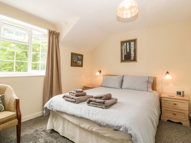 A bedroom with a double bed, bedside tables, lamps, a window with curtains, and an armchair at Wye Valley Cottage in Symonds Yat