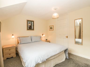 A bedroom with a double bed bedside tables wall sconces and a mirror on the wall at Wye Valley Cottage in Symonds Yat