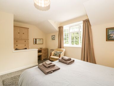 A bedroom with a bed and folded towels on it a wooden dresser a chair and a window with curtains at Wye Valley Cottage in Symonds Yat