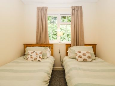 A bedroom with two single beds with animal print pillows and a window with closed curtains at Wye Valley Cottage in Symonds Yat