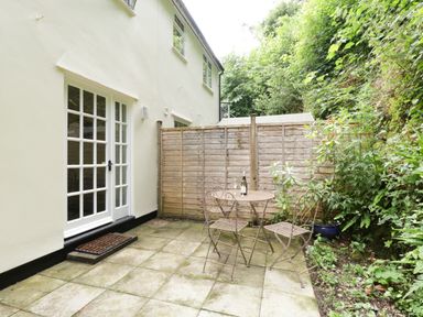 A small patio with a table and four chairs outside a house with glass doors surrounded by greenery at Wye Valley Cottage in Symonds Yat