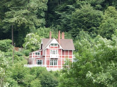 A red and white house surrounded by trees and greenery at Wye Valley Cottage in Symonds Yat