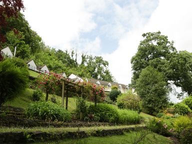 A garden with flowering plants trees and a wooden pergola near houses on a hillside at Wye Valley Cottage in Symonds Yat