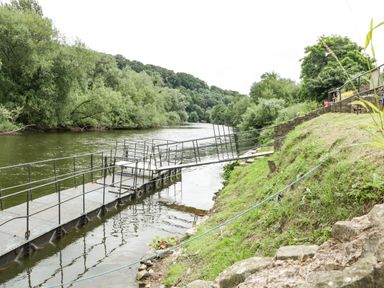A metal dock extending into a river with a grassy bank and trees along the water at Wye Valley Cottage in Symonds Yat