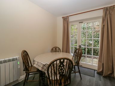 A dining area with a round table covered by a checked tablecloth and four wooden chairs near glass patio doors with curtains at Wye Valley Cottage Symonds Yat